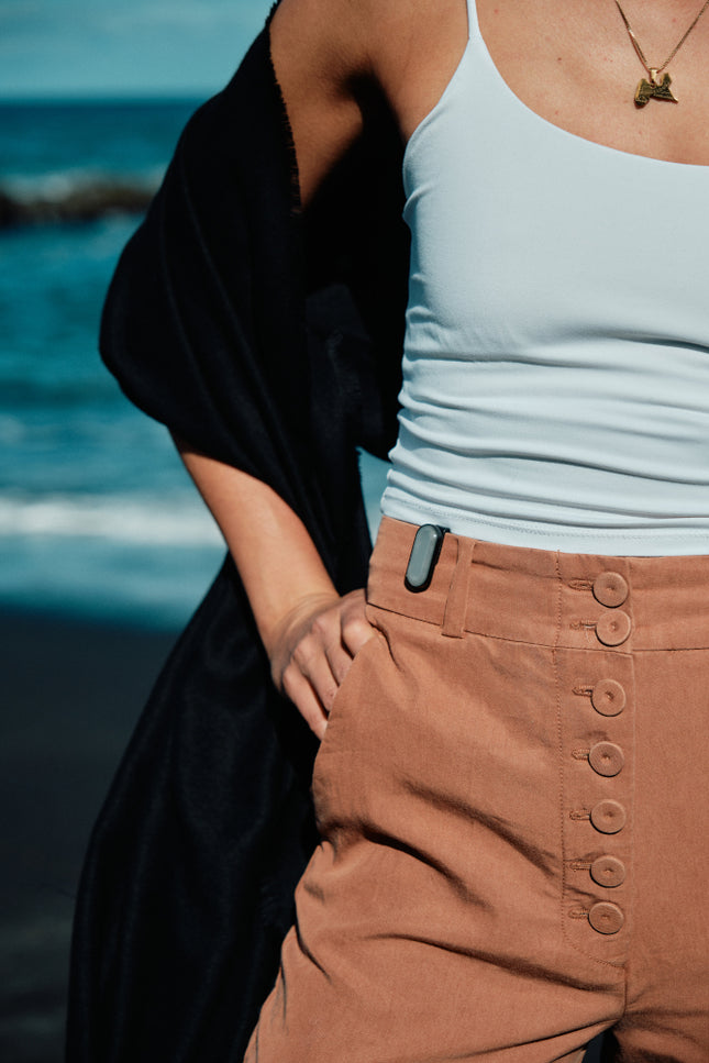 Close-up of woman wearing orange high-waist pants with sun-a-wear UV tracker attached to the waist as part of her apparel 